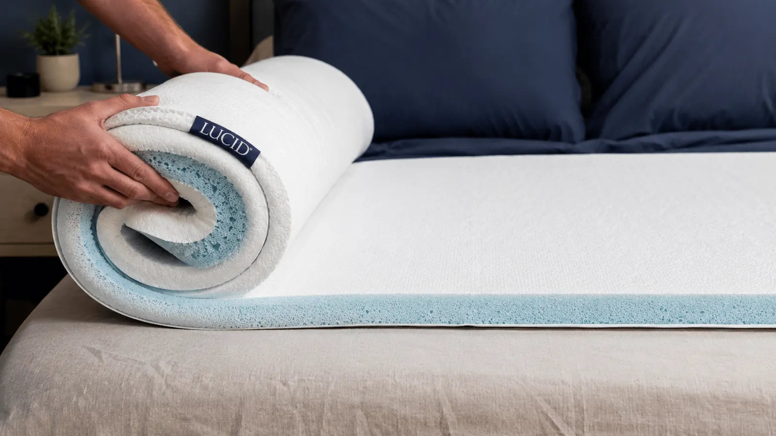 Hands unrolling a thick gel memory foam mattress topper onto a bed frame