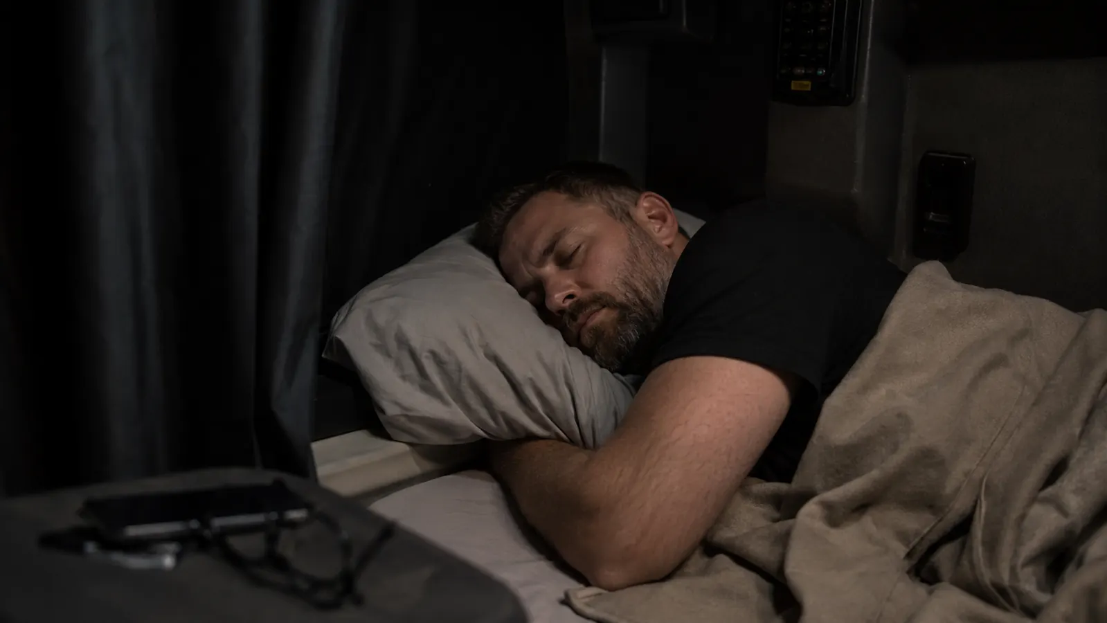 Person sleeping soundly in a dark truck sleeper cab with blackout curtains drawn