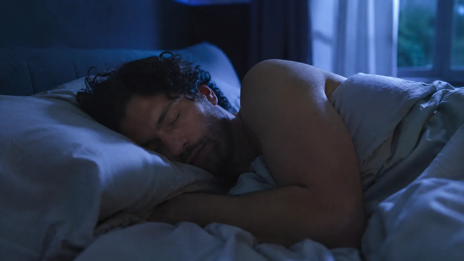 Person sleeping comfortably on a cool bed in a dark room, white sheets, relaxed expression, no sweat