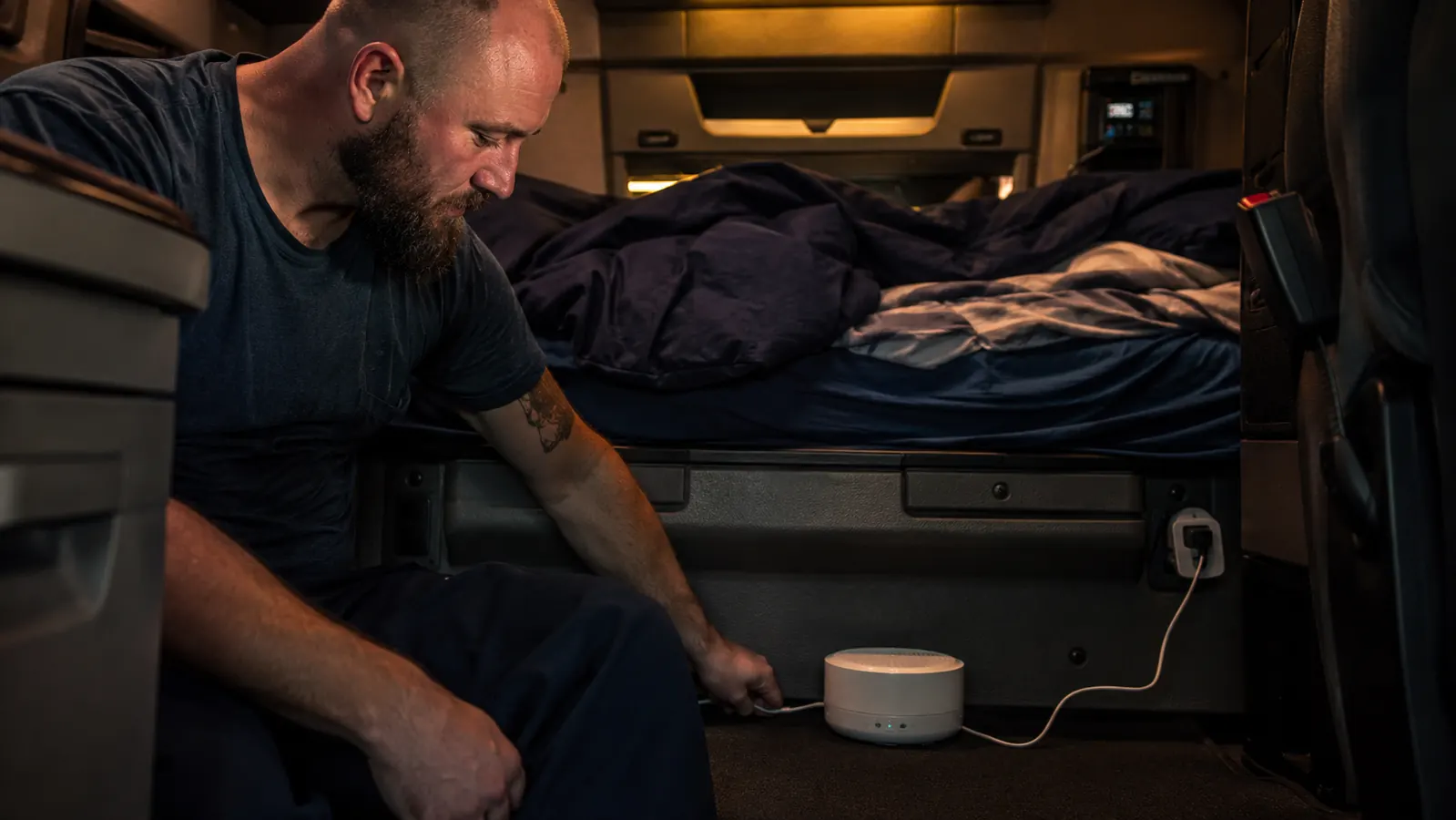 Yogasleep Dohm on the floor of a semi truck sleeper cab, power cord running to a USB adapter, bunks visible in background